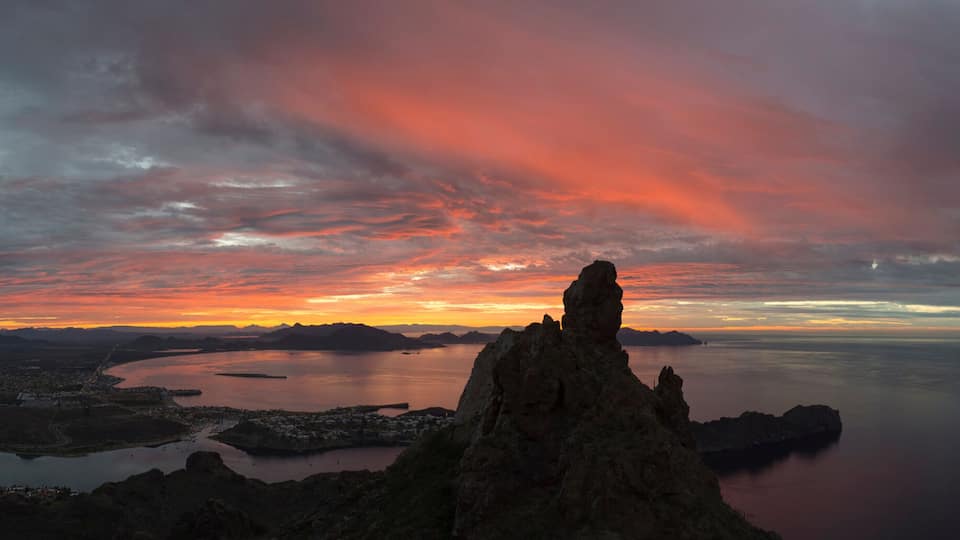 A coastal landscape with a prominent rock formation, a calm sea, and a sunset with clouds.