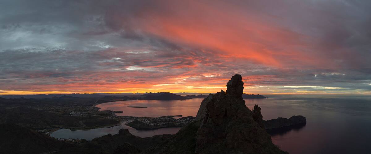A coastal landscape with a prominent rock formation, a calm sea, and a sunset with clouds.