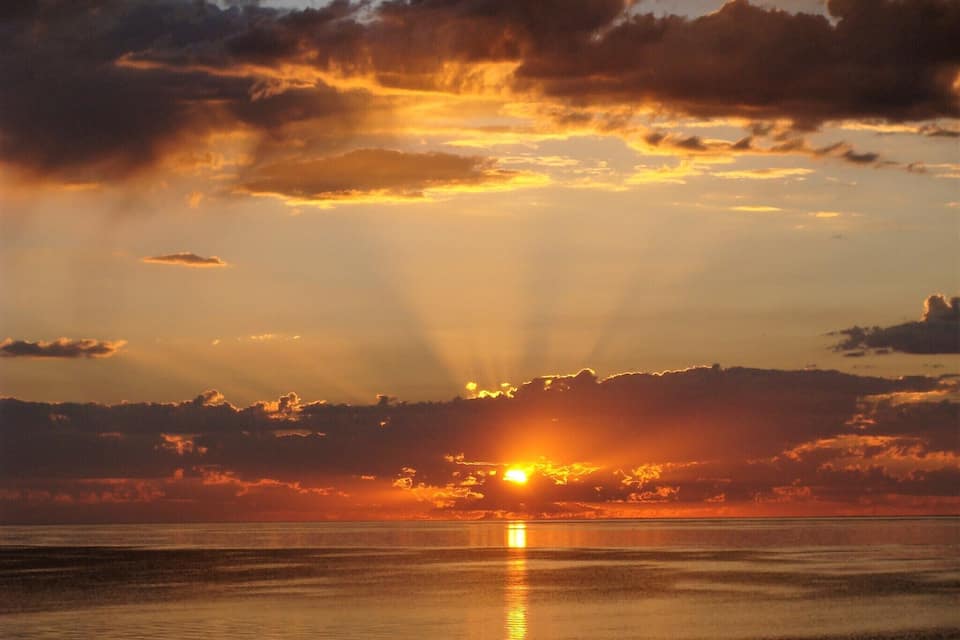 Un atardecer sobre un mar tranquilo con nubes que reflejan la luz del sol.