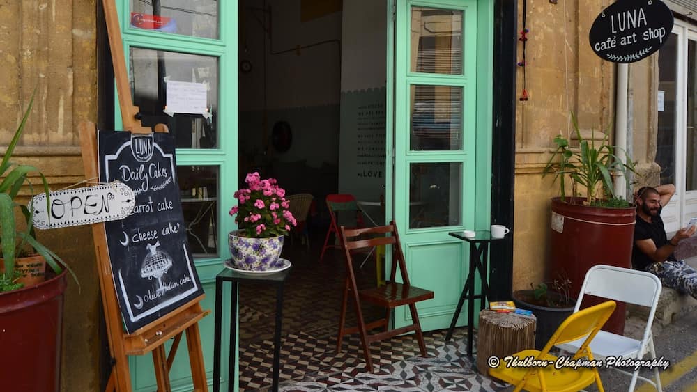 A café art shop with a chalkboard sign listing daily cakes and a potted plant.