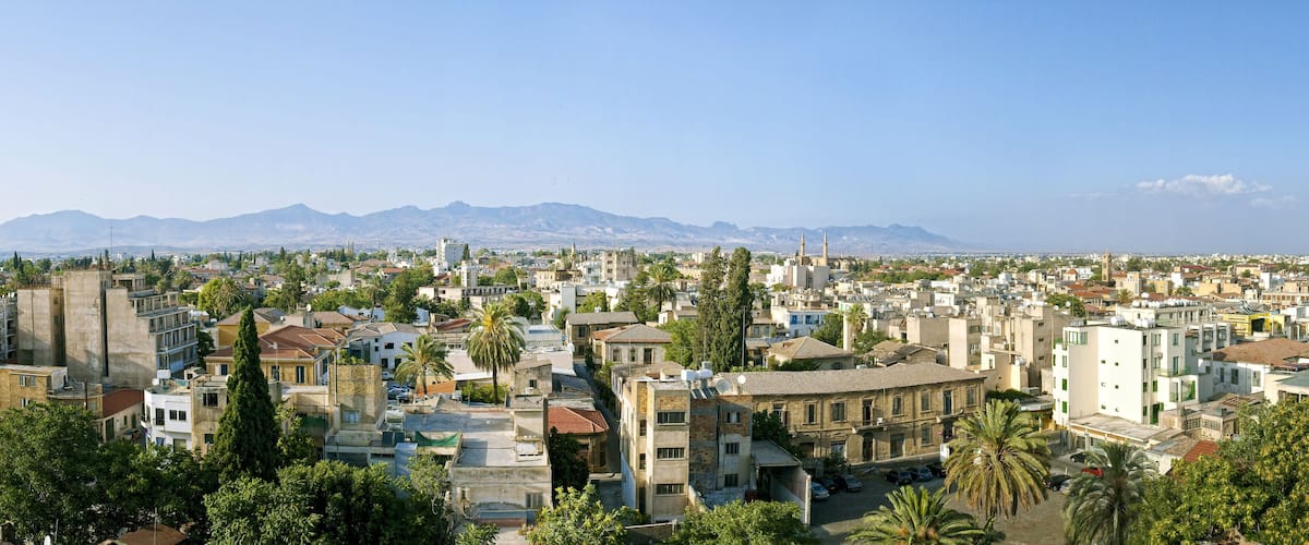 A cityscape with a mix of modern and traditional buildings, palm trees, and mountains in the background.