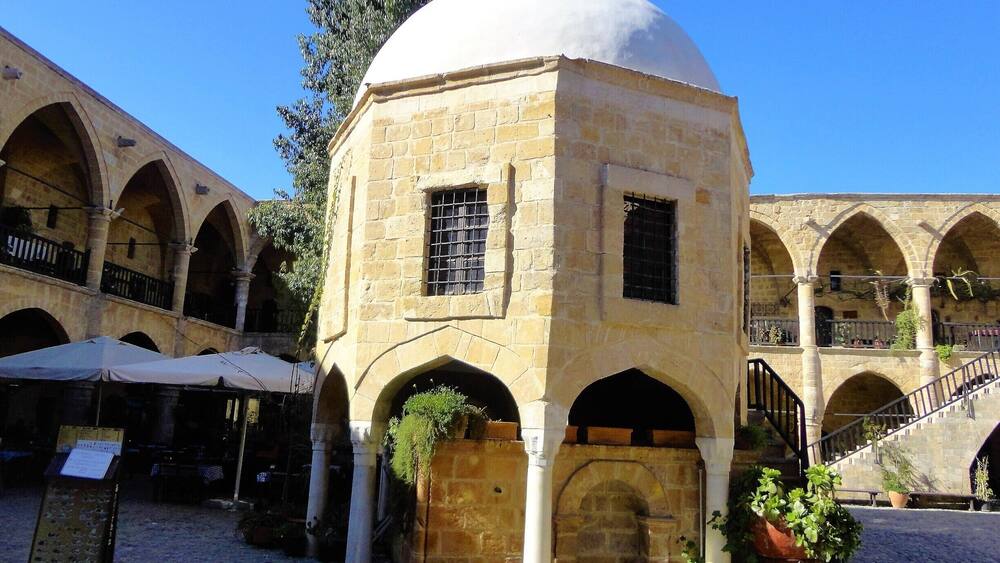 A historic building with a dome and arches, surrounded by a courtyard with potted plants and a cobblestone floor.
