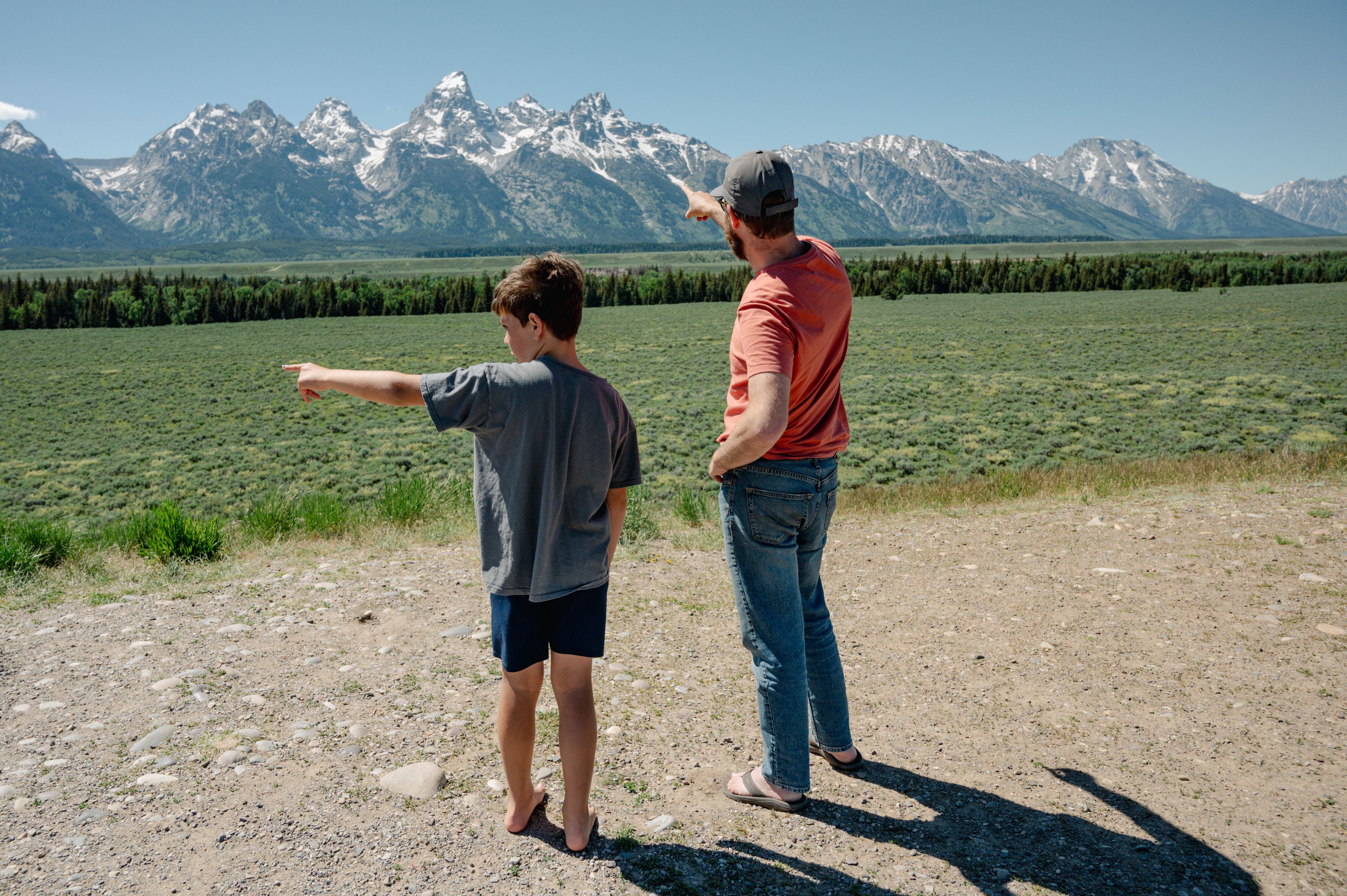 Father and son standing and pointing at Teton mountain range