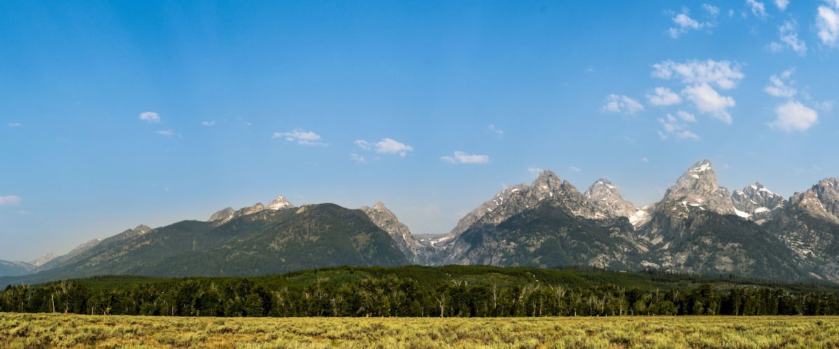 A mountain range with a forested valley and a clear blue sky.