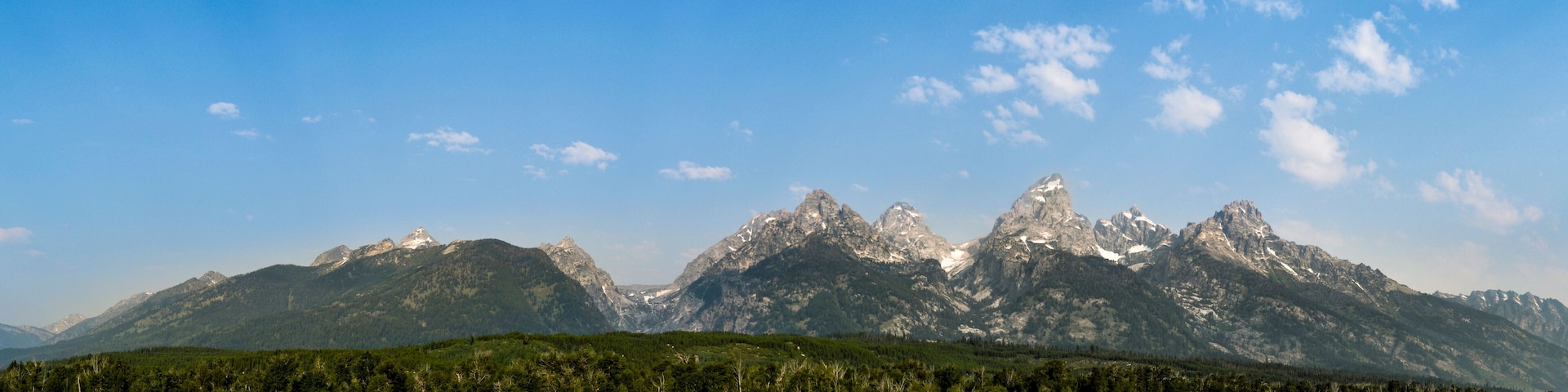 A mountain range with a forested valley and a clear blue sky.
