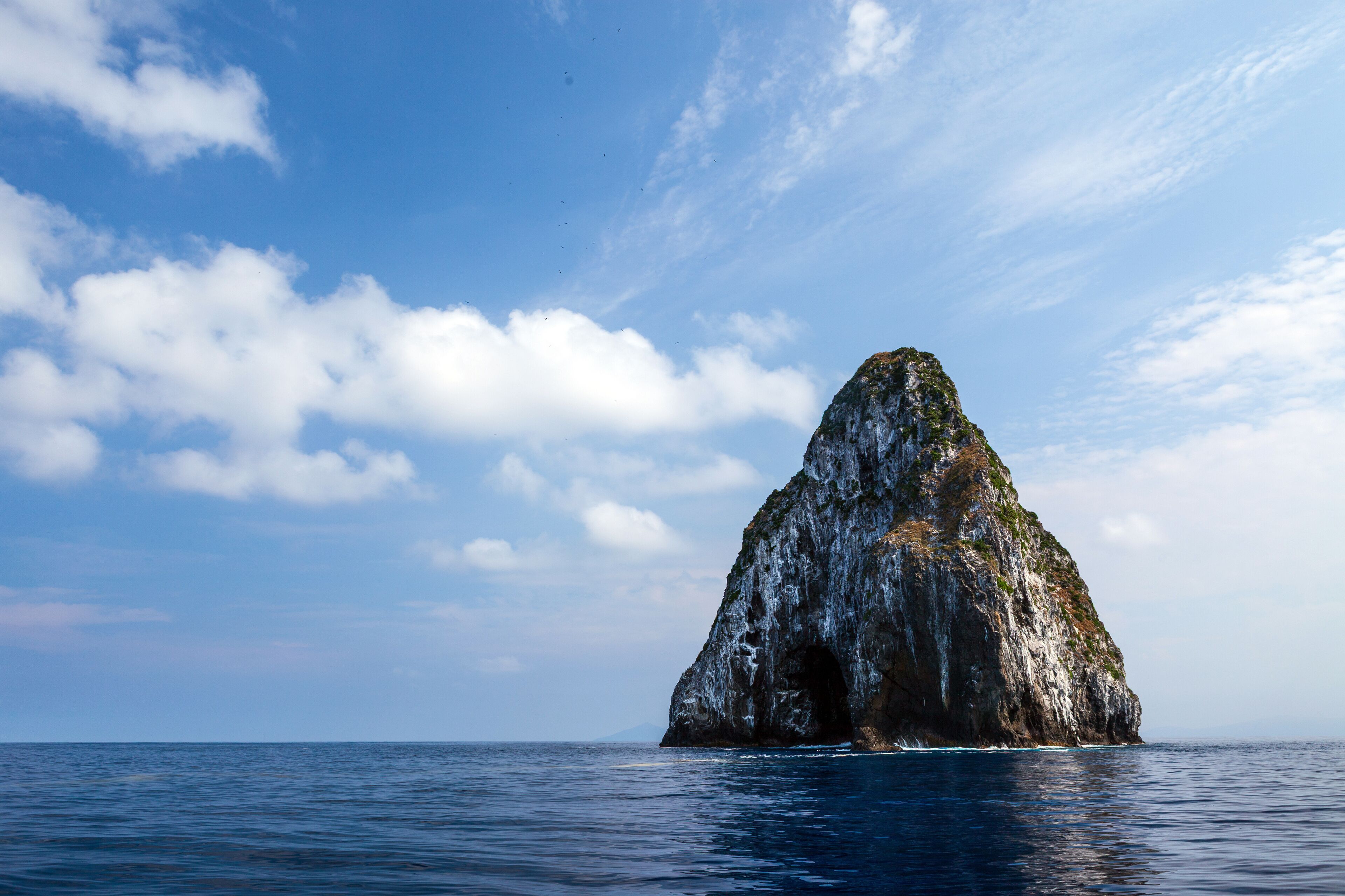 A large rock formation in the ocean with a clear sky.