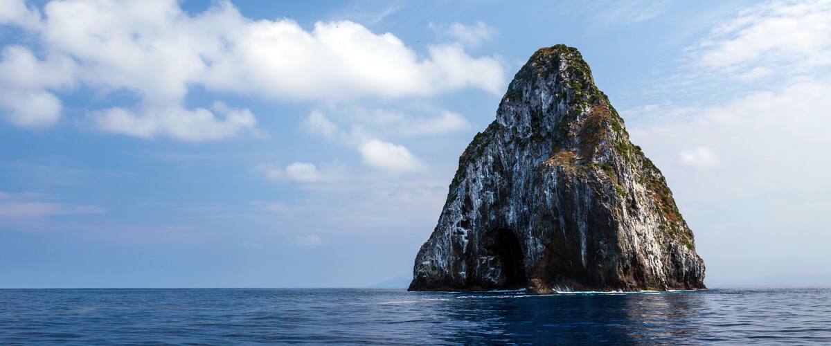 A large rock formation in the ocean with a clear sky.