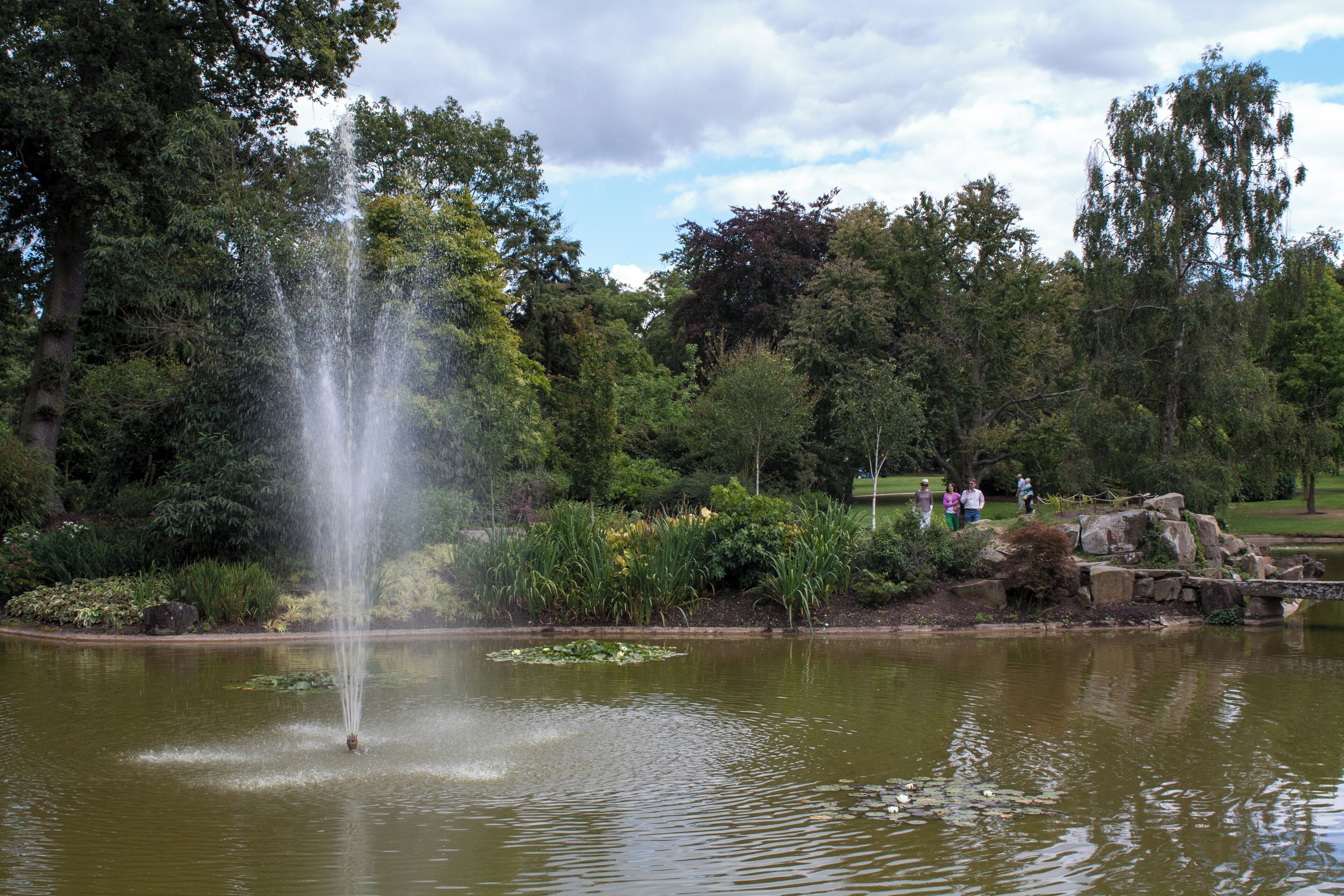 A fountain in a park with trees and a small bridge.