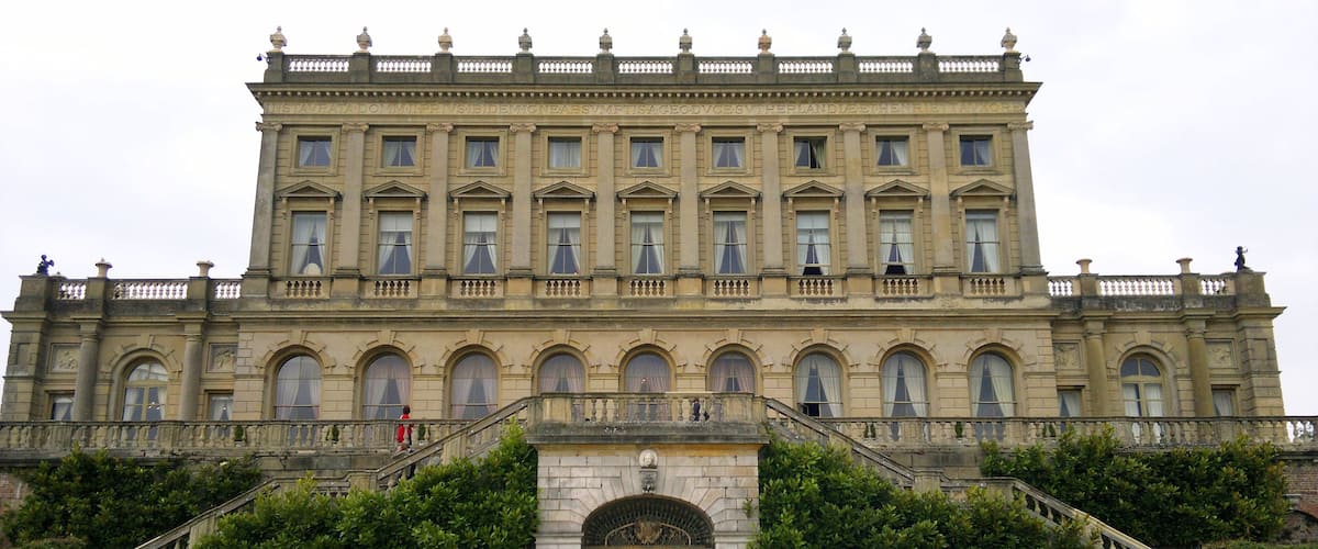 A grand, historic building with a symmetrical facade, large windows, and a central entrance with a decorative gate.