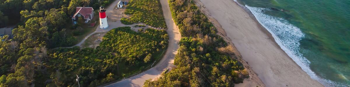An aerial view of a coastal area with a lighthouse, beach, and surrounding forest.