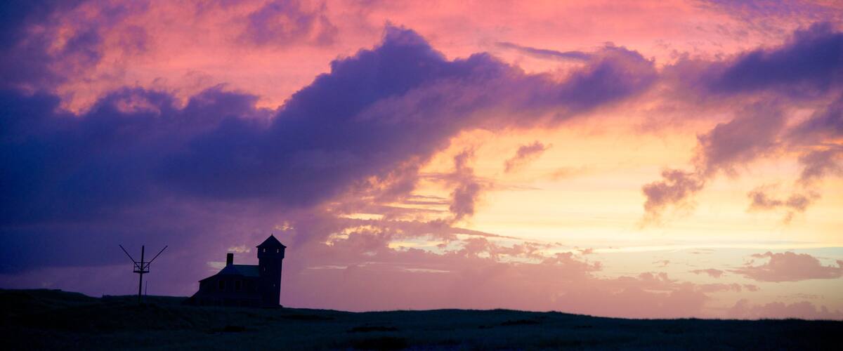 A house with a tower silhouetted against a vibrant sunset sky.