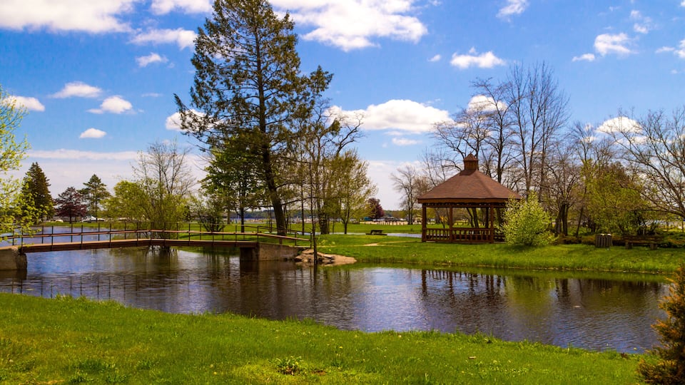 A park with a pond, a gazebo, a bridge, and trees.
