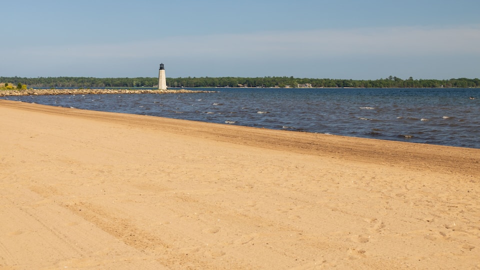 A sandy beach with a lighthouse in the distance.