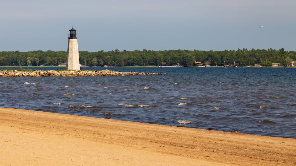 A lighthouse on a rocky outcrop, a sandy beach, and a forested shoreline.