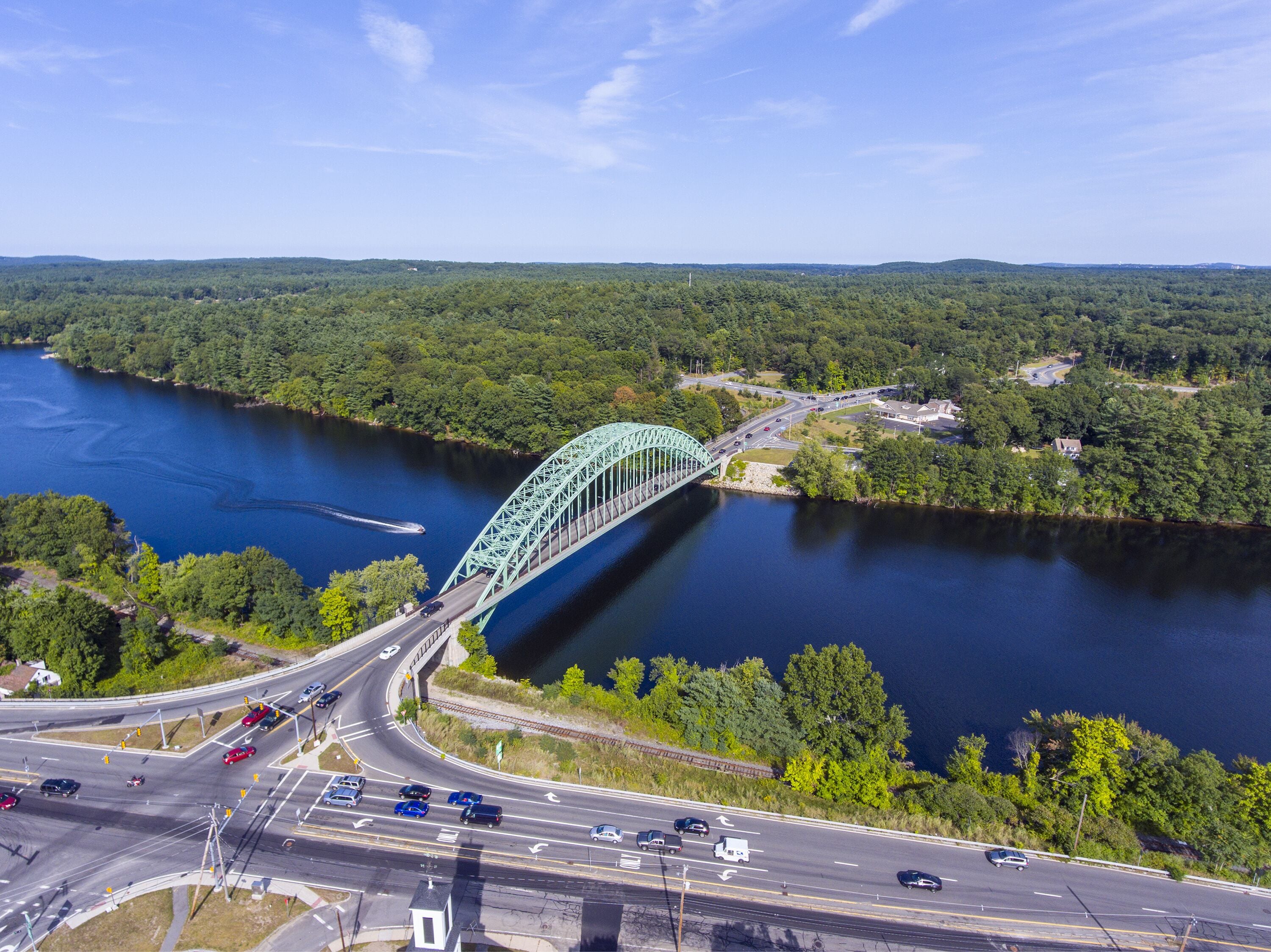 Un puente verde sobre un río, con vegetación circundante y una autopista.