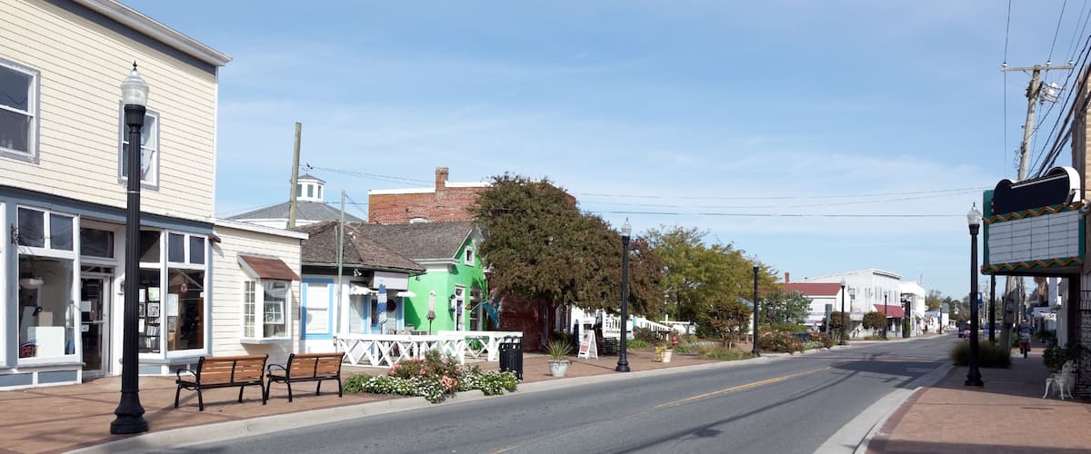 A quiet street lined with buildings, a bench, and a white fence.