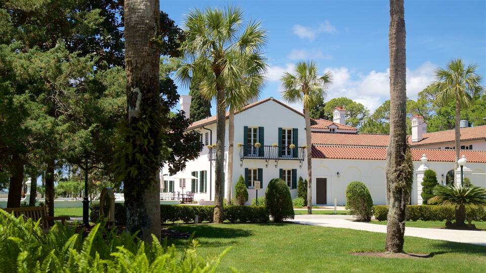 A white building with green shutters, surrounded by palm trees and a well-maintained lawn.