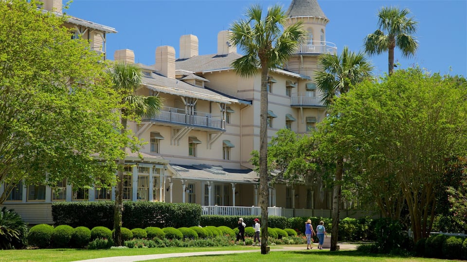 A large, historic building with a tower, surrounded by lush greenery and a well-maintained garden.