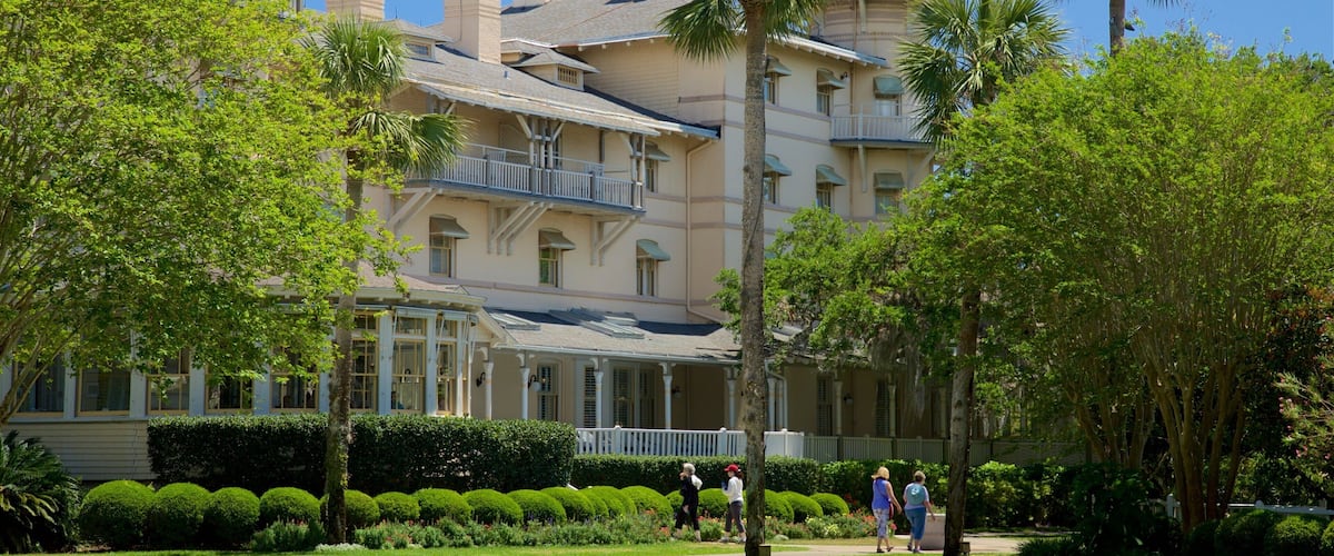 A large, historic building with a tower, surrounded by lush greenery and a well-maintained garden.