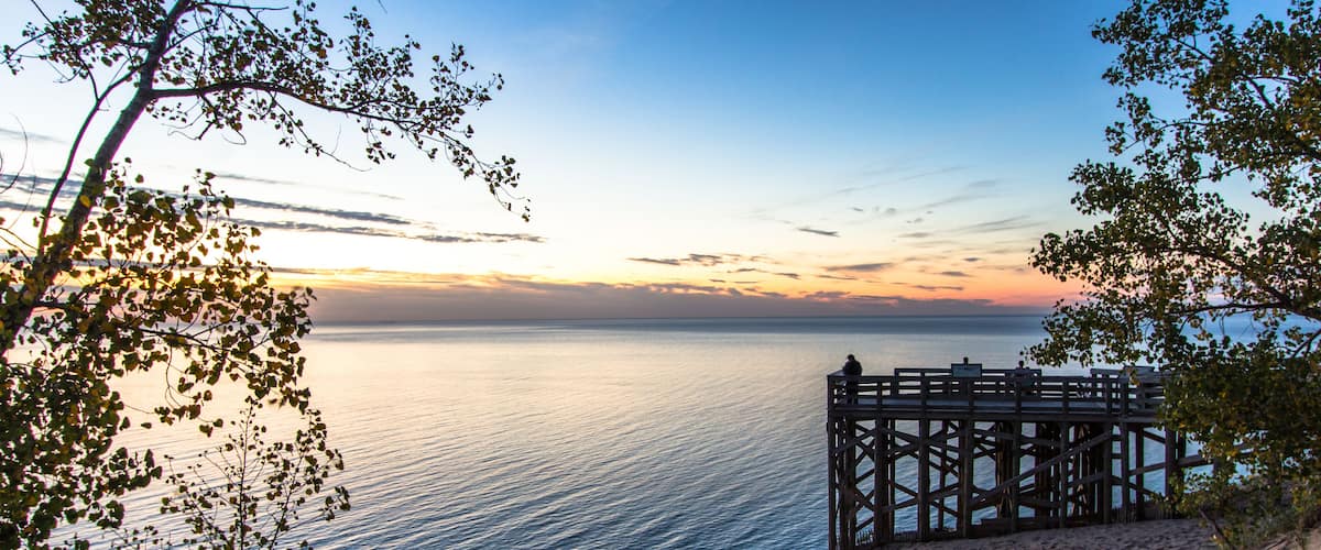 A wooden pier extending into a calm sea, surrounded by sandy beach and trees.