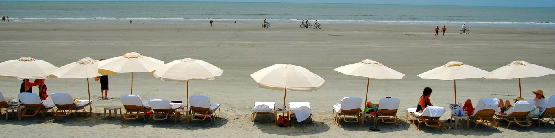 A beach with rows of sun loungers and umbrellas, a calm sea, and a clear sky.