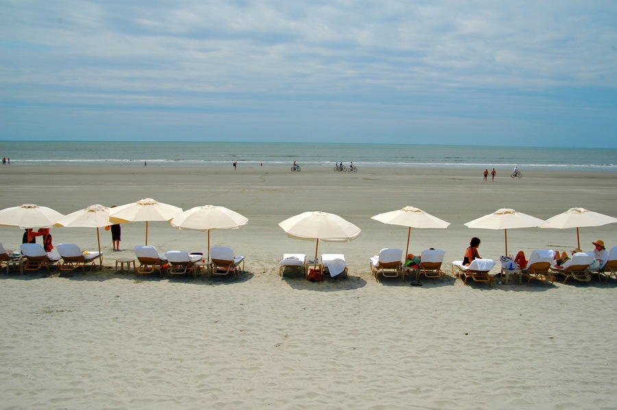 A beach with rows of sun loungers and umbrellas, a calm sea, and a clear sky.