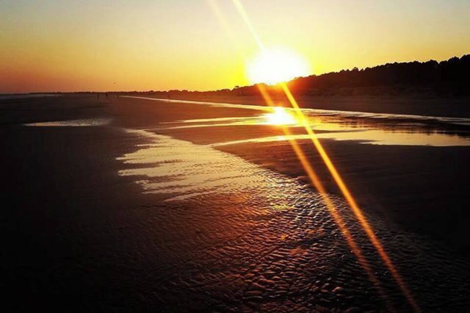 Um pôr do sol sobre uma praia, com o sol refletindo na água.
