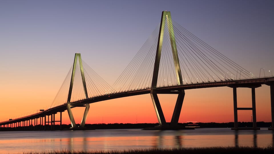 A bridge with a distinctive cable design, spanning over a body of water during sunset.