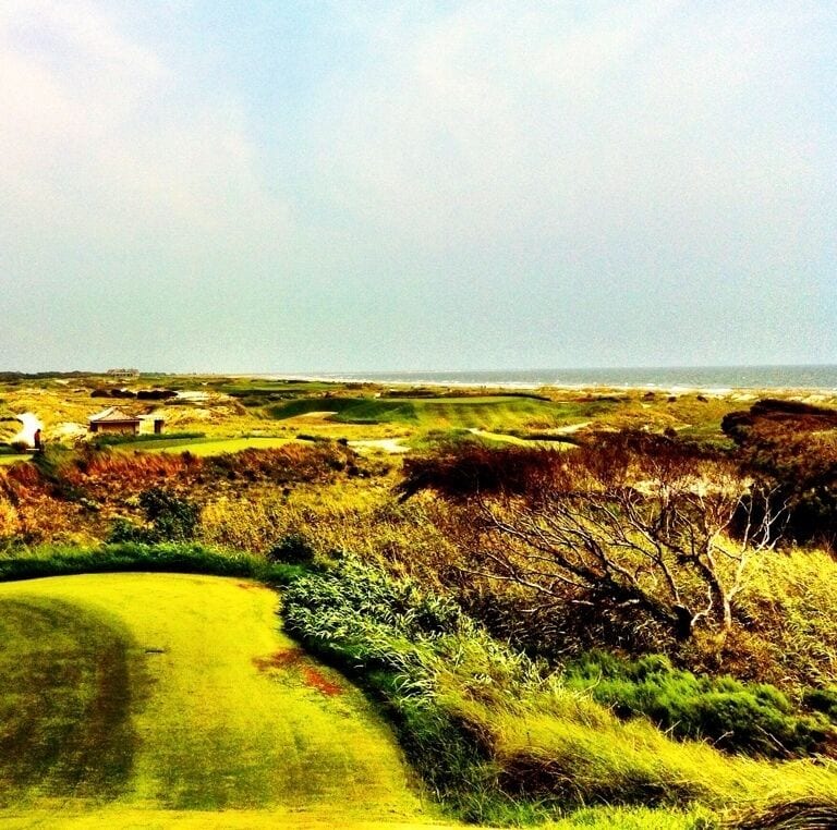 Ein Golfplatz mit einem Wasserhindernis, einem Bunker und weiter Aussicht auf den Ozean.