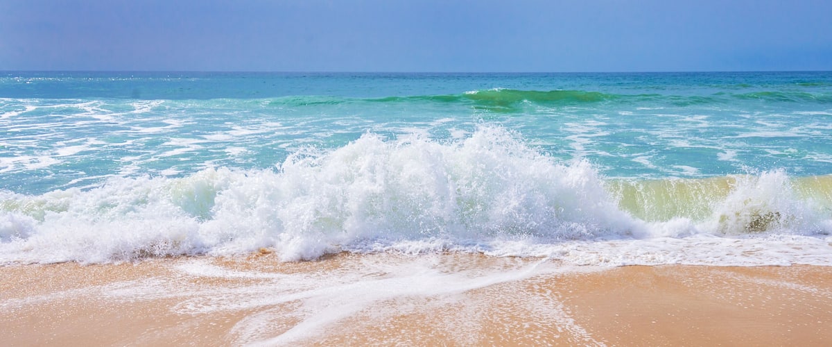 A beach with waves crashing onto the shore under a clear sky.