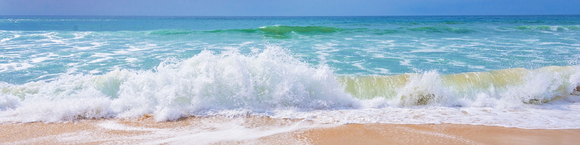 A beach with waves crashing onto the shore under a clear sky.