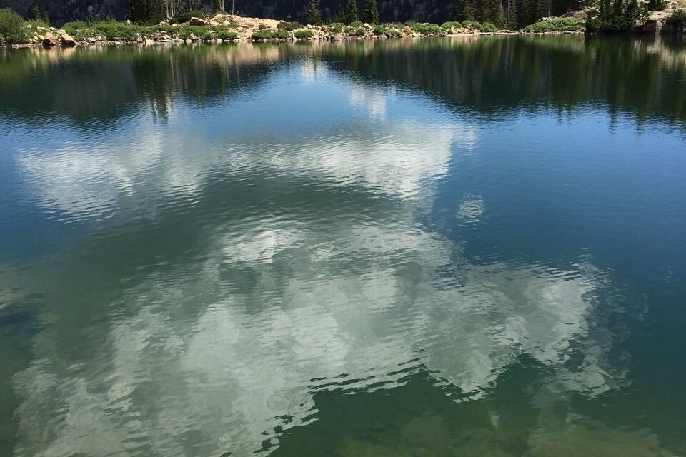 Um lago de montanha límpido refletindo o céu e a floresta ao redor.
