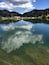 A clear mountain lake with reflections of the sky and surrounding forest.