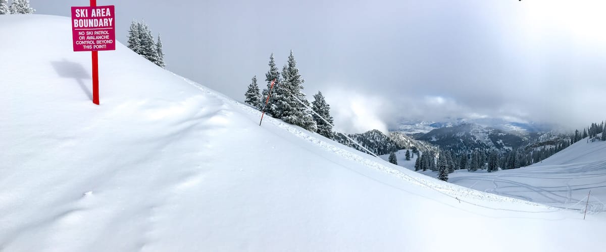 A snowy ski slope with a sign indicating the boundary of the ski area.