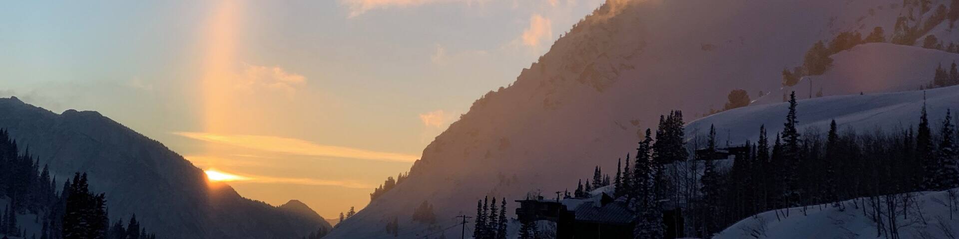 A mountain landscape with a sunrise, snow-covered slopes, and a clear sky.