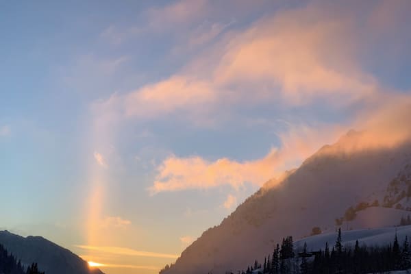 A mountain landscape with a sunrise, snow-covered slopes, and a clear sky.