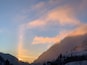 A mountain landscape with a sunrise, snow-covered slopes, and a clear sky.