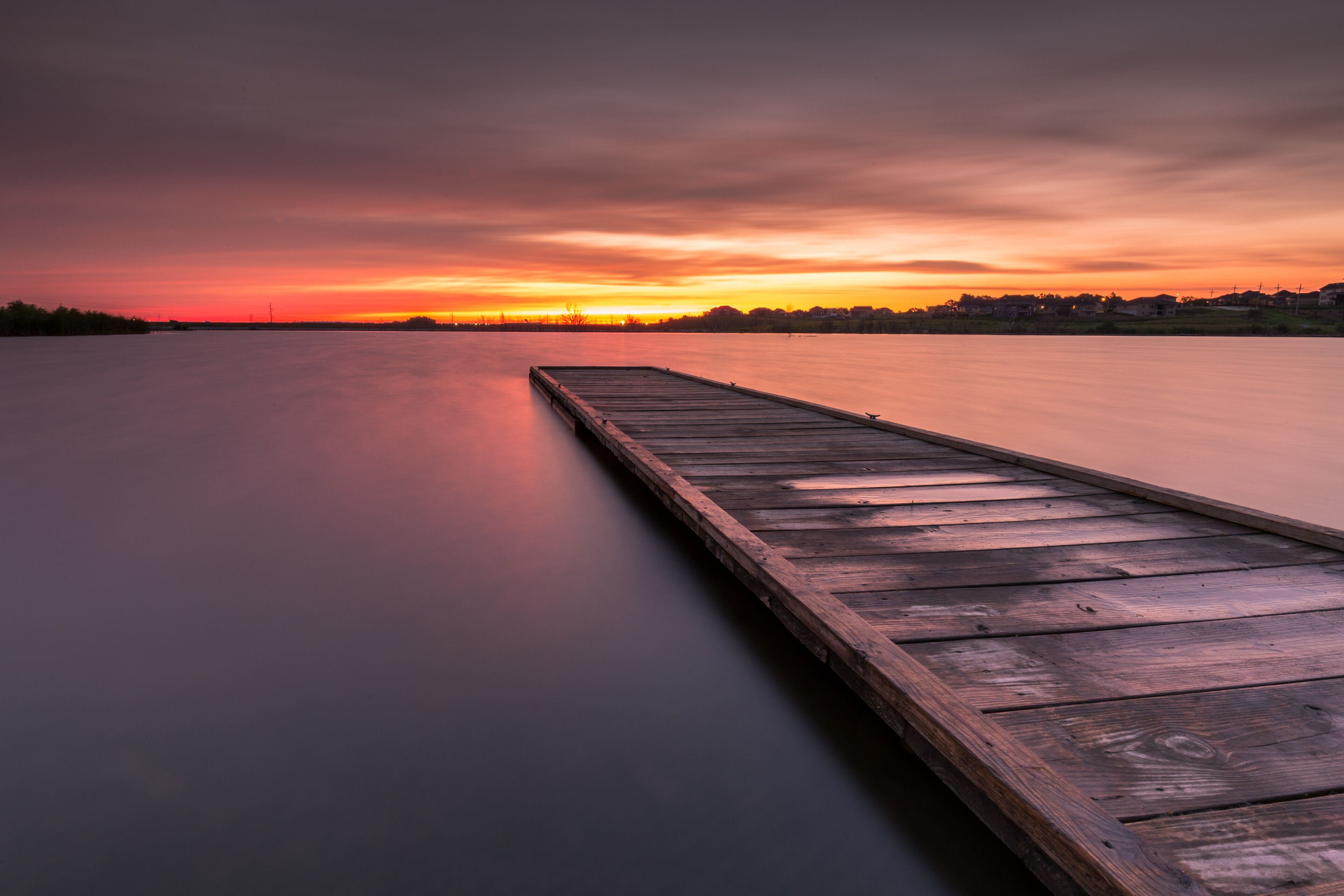 Un muelle de madera que se adentra en una masa de agua tranquila al atardecer.