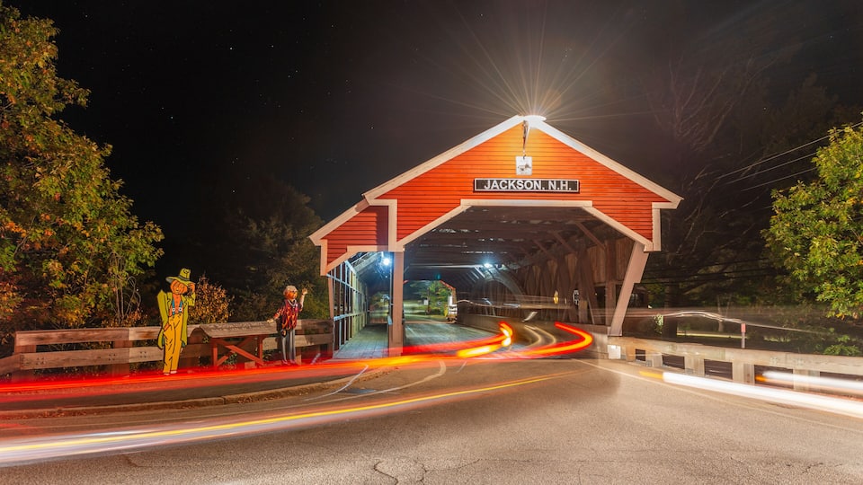 A covered bridge with a sign reading "JACKSON, N.H." at night.