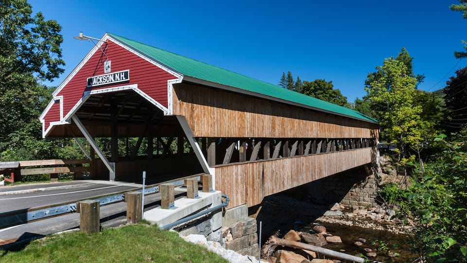 A wooden covered bridge with a green roof and a sign reading 'Jackson, N.H.'