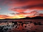 Un atardecer sobre una costa rocosa con una montaña al fondo.