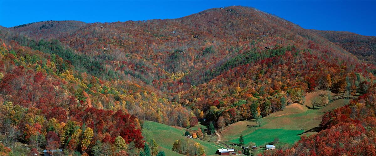 A mountainous landscape with autumn foliage, a small settlement, and a clear blue sky.