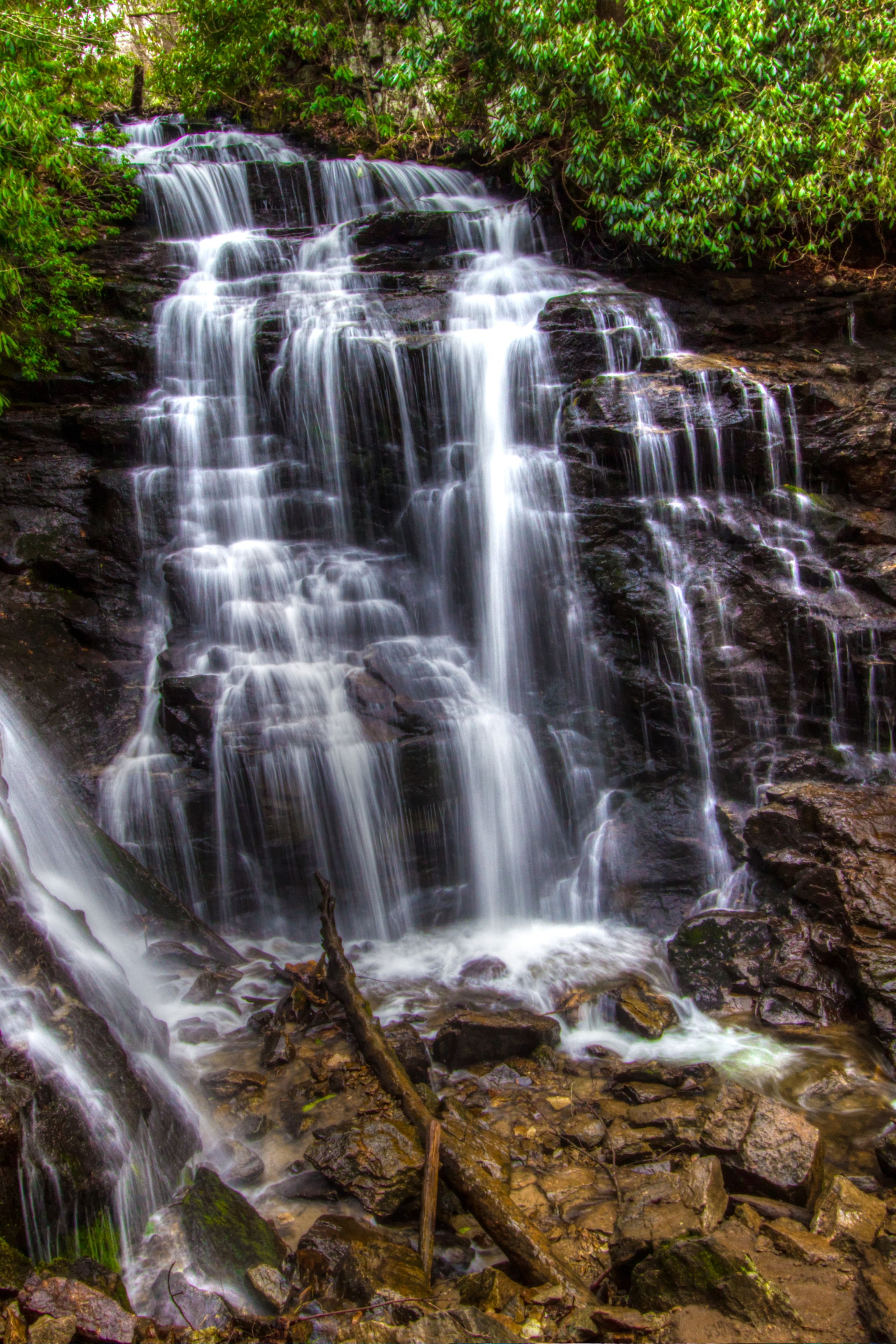 A multi-tiered waterfall cascading over rocky terrain surrounded by lush greenery.