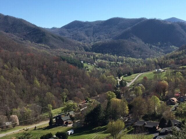 A valley with houses, a winding road, and mountains in the background.