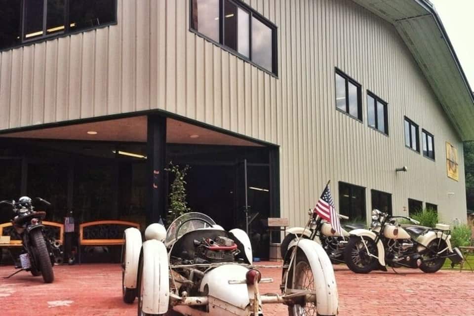 A building with a large garage door, a parked motorcycle with a sidecar, and another motorcycle in the background.