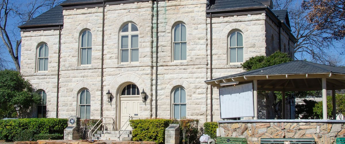 Un edificio de piedra grande con una torre de reloj, ventanas arqueadas y una placa con la fecha.