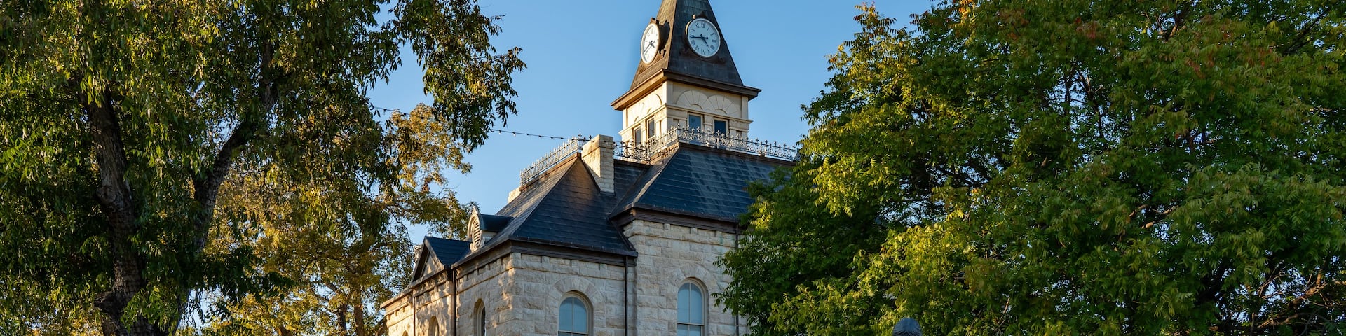 A historic church with a clock tower, surrounded by trees and a statue.