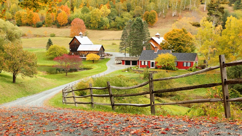 A rural landscape with barns, a wooden fence, and autumn foliage.