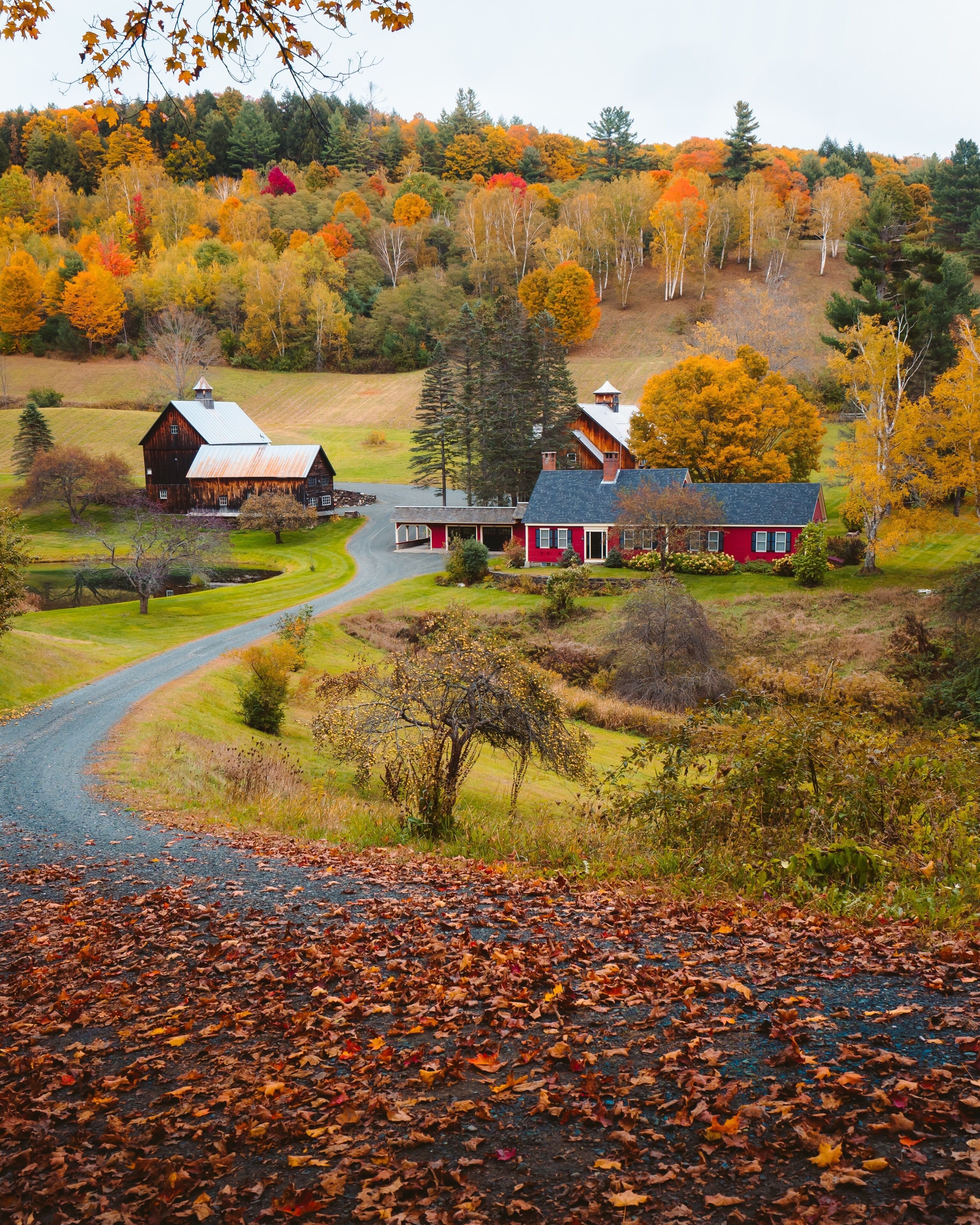Paisaje rural con graneros, una casa roja y follaje otoñal.