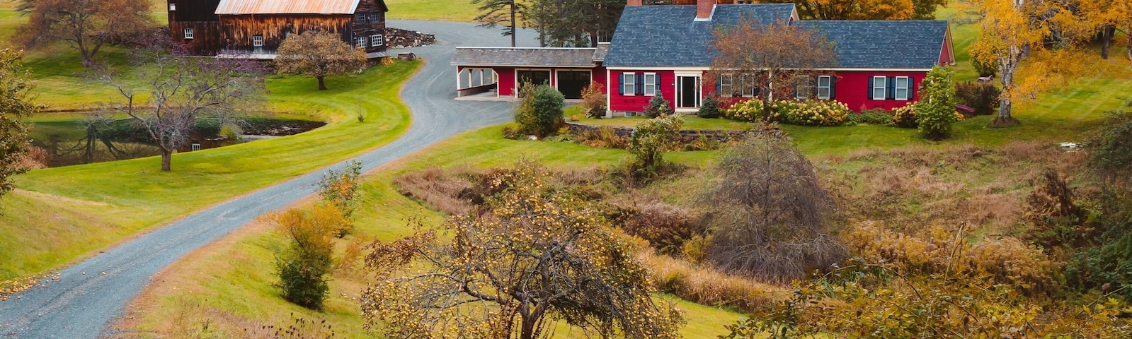 Paisaje rural con graneros, una casa roja y follaje otoñal.